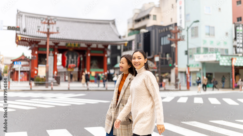 Fototapeta premium Asian woman friends crossing street crosswalk with crowd of people during travel together at Asakusa, Tokyo, Japan in autumn. Attractive girl enjoy urban outdoor lifestyle travel on holiday vacation.