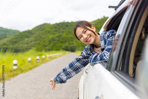 Young Asian woman enjoy outdoor lifestyle travel nature road trip and camping on summer holiday vacation. Happy attractive girl sitting in driving car with pull her face and hand out of car window.