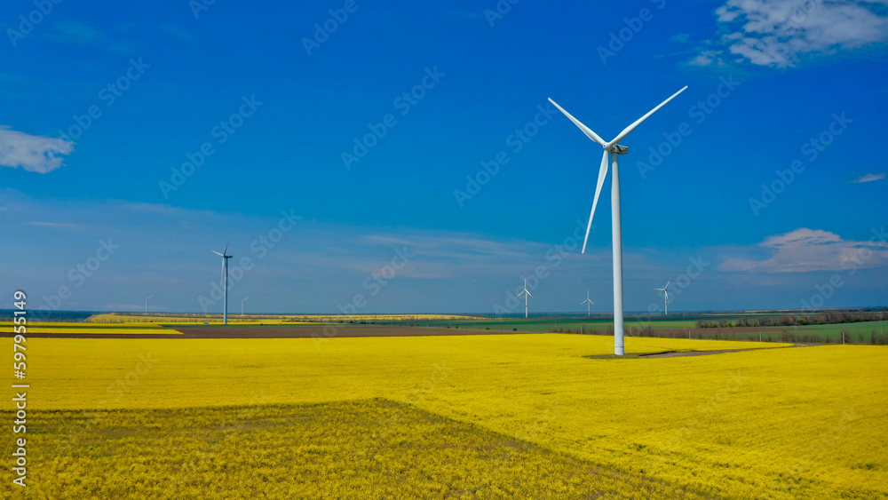 Aerial view from flying drone at windmills on yellow spring fields on a beautiful spring day. Environment protection. Renewable alternative energy sources. Aerial view from flying drone at windmills on yellow spring fields on a beautiful spring day. Environment protection. Renewable alternative energy sources.