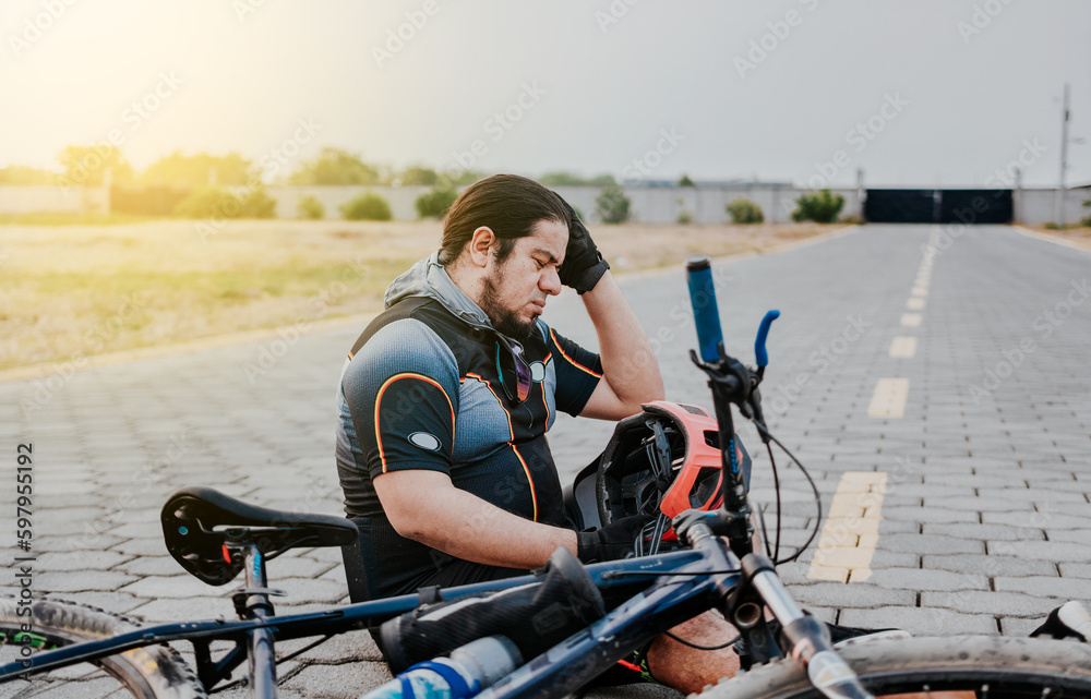 Male cyclist sitting with headache. Cyclist on the pavement with a headache. Concept of cyclist suffering with migraine