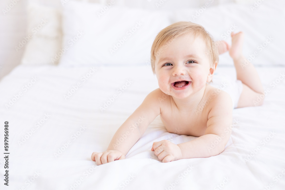 laughing or smiling baby boy blond with big eyes close-up or portrait in a crib at home, the concept of children's goods and accessories