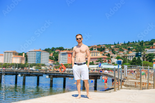 Handsome young man on sea beach on the background of the sea and the city. male body torso. © Ivan