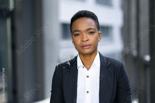 Portrait business woman with short black hair looking at camera while standing outdoors near the office building