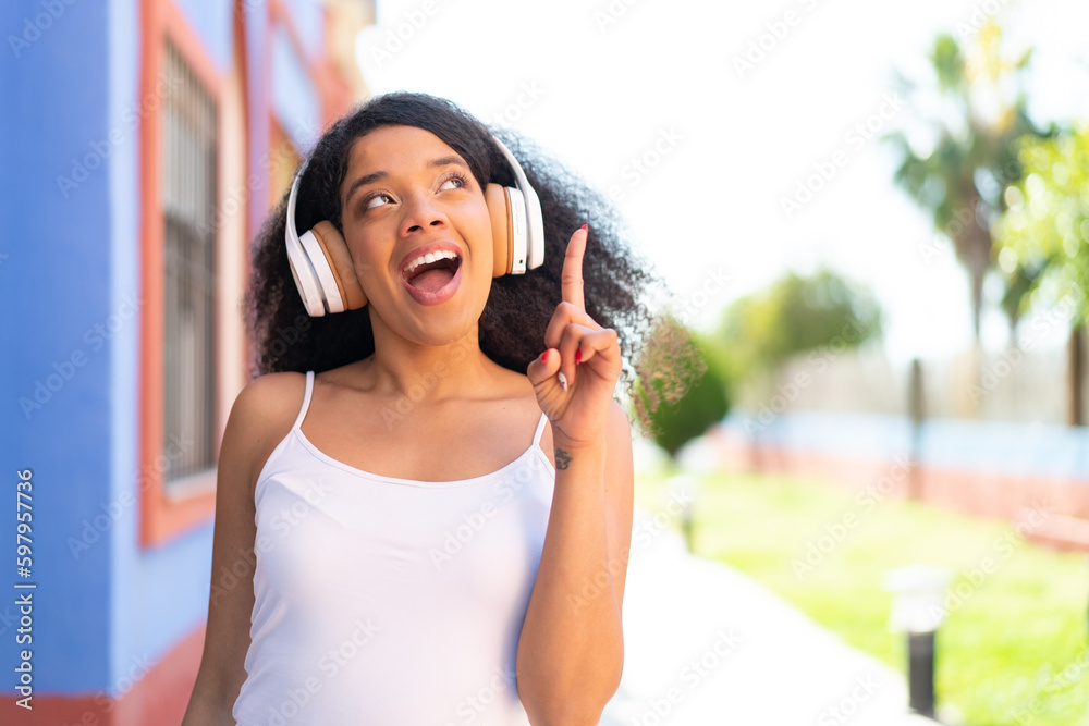 Young African American woman with headphones at outdoors intending to realizes the solution while lifting a finger up