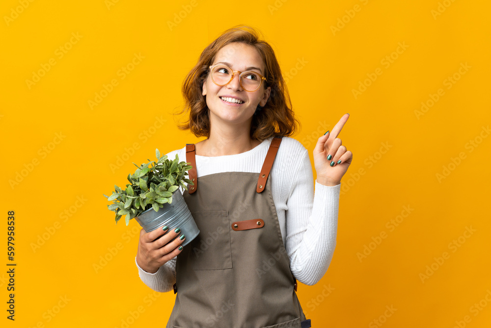 Young Georgian woman holding a plant isolated on yellow background pointing up a great idea Young Georgian woman holding a plant isolated on yellow background pointing up a great idea