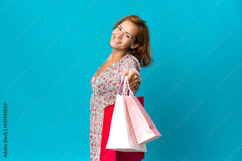 Young Georgian woman with shopping bag isolated on blue background holding shopping bags and giving them to someone Young Georgian woman with shopping bag isolated on blue background holding shopping bags and giving them to someone