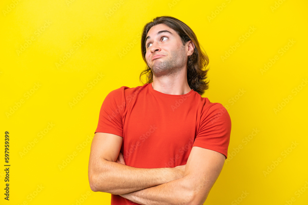 Caucasian handsome man isolated on yellow background making doubts gesture while lifting the shoulders