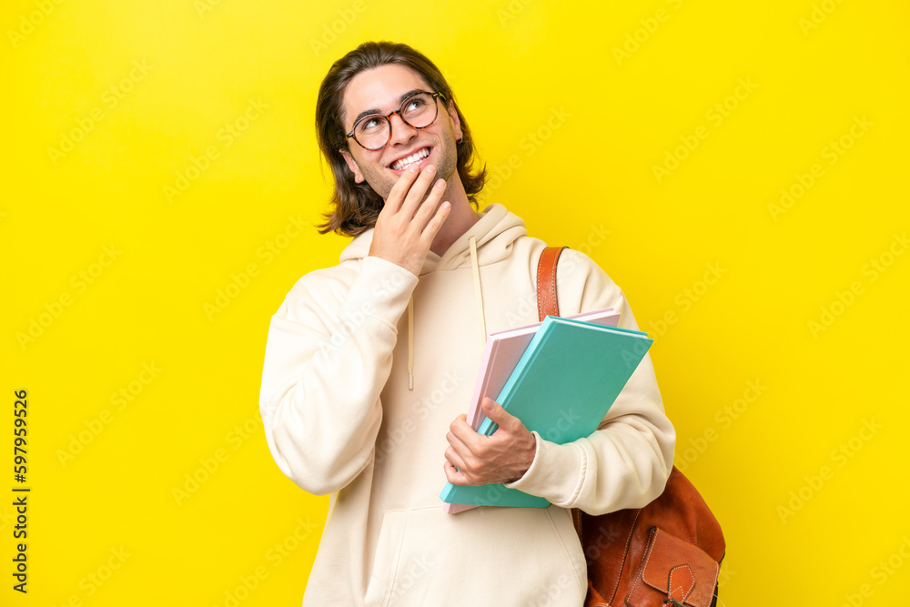 Young student handsome man isolated on yellow background looking up while smiling Young student handsome man isolated on yellow background looking up while smiling