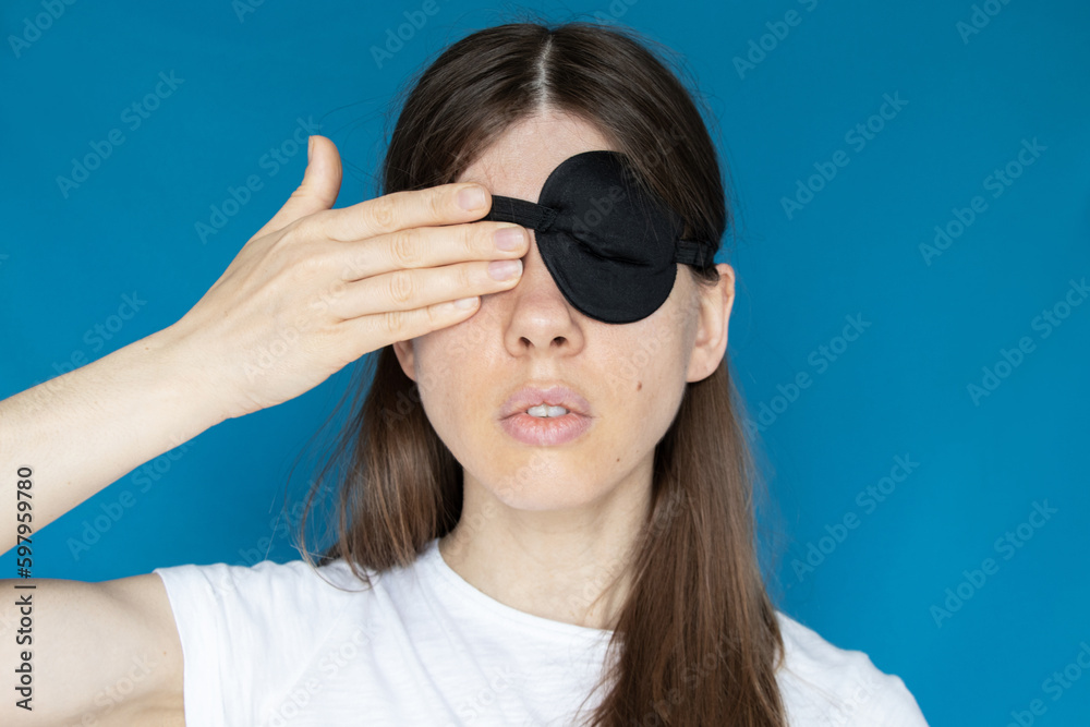 A girl with a bandage on one eye and the other eye closed with her hand on a blue background, don't see, don't look, it's a secret A girl with a bandage on one eye and the other eye closed with her hand on a blue background, don't see, don't look, it's a secret
