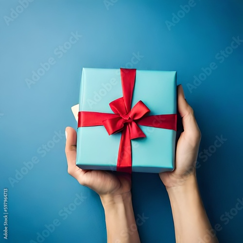 Gift box with red ribbon and bow on blue background. Holiday gift with copy space. Birthday or anniversary present holding in hands, flat lay, top view. giftbox concept.