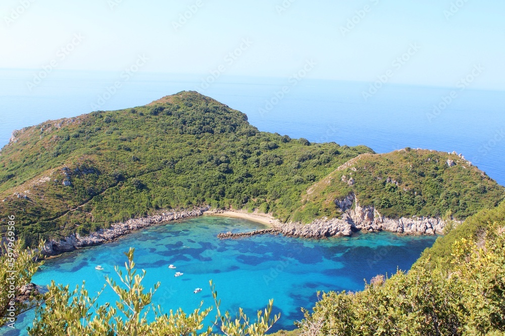Top view of Porto Timoni, Greece. The sky is very blue on a sunny day, the sea water is turquoise and the trees in the hills are very green. This is a very beautiful view point in the rocks