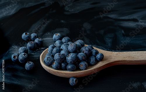 Fresh Blueberries in a wooden spoon on dark background, top view.