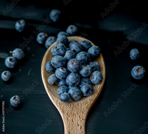 Fresh Blueberries in a wooden spoon on dark background, top view.