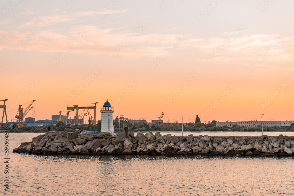 Sunset landscape with the Genoese lighthouse that has a blue roof, from the pier made of rocks, in a port on the Black Sea.