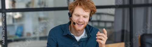 Obraz na płótnie Smiling man call center worker in headphones is working at modern office. Portrait of a happy male support employee, smiles w salonie