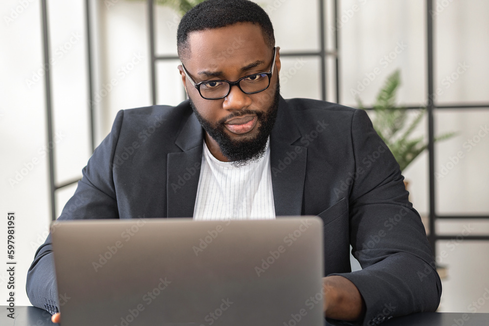 Portrait of a confident Afro American businessman, executive, CEO working using laptop sitting at workplace in office Portrait of a confident Afro American businessman, executive, CEO working using laptop sitting at workplace in office