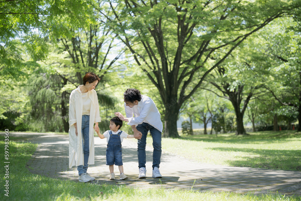 公園をお散歩する仲良し家族 新緑の中手をつなぐファミリーのイメージ 広角 右にコピースペースあり