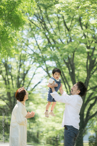 新緑の中高い高いをしてもらう子どもと幸せそうな家族 縦 © kapinon