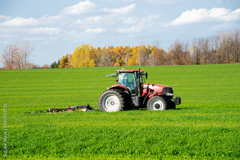 Obraz premium Close-up larger farm tractor with rotary cutter trailer on farmland meadow field, colorful fall foliage, cloud blue sky South Lockport, Niagara County, Upstate New York, USA