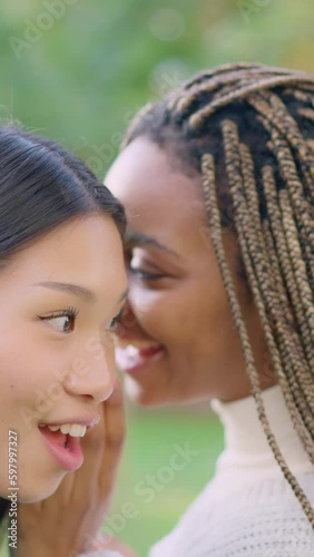 African woman tells friend a secret in her ear outdoors