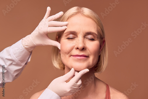 Leinwand Poster Portrait of an older adult woman with closed eyes on a beige background