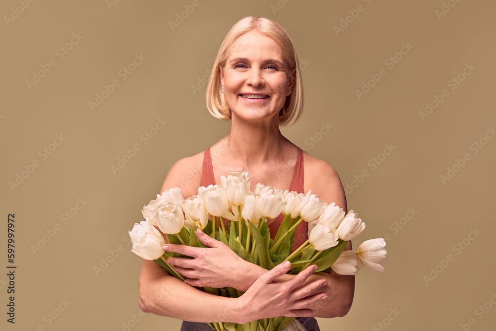 Women's beauty and spring.Portrait of a beautiful middle-aged woman holding a bouquet of white tulips and smiling on an olive background.