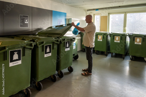 Stockholm, Sweden A man throws garbage in a super clean and organised garbage room in a residential housing complex.The labels denote type of waste in Swedish. photo