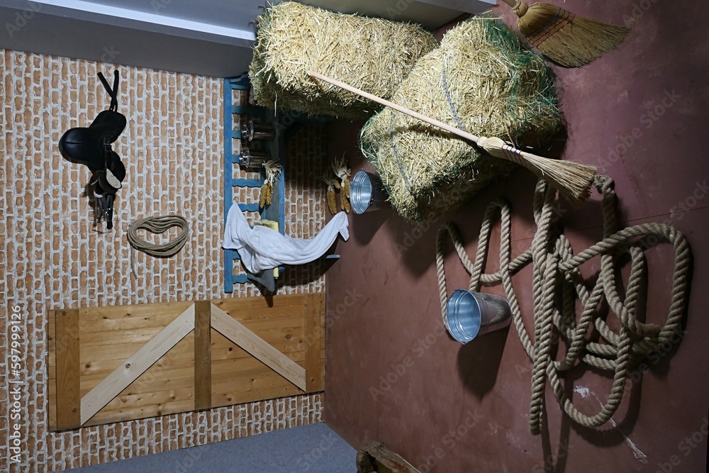 Stable interior with haystacks, broom, rope, buckets and horse saddle ...