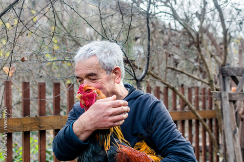 portrait of a farmer man holding a rooster with his hands