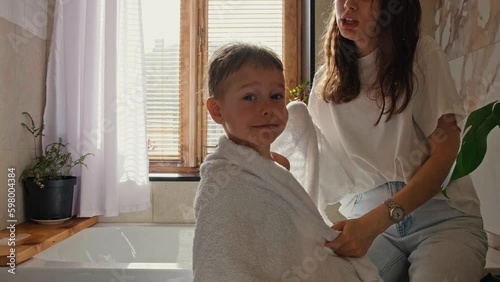 A young mother wipes her son with a towel after a shower. Mom takes care of her son. Morning shower with baby.