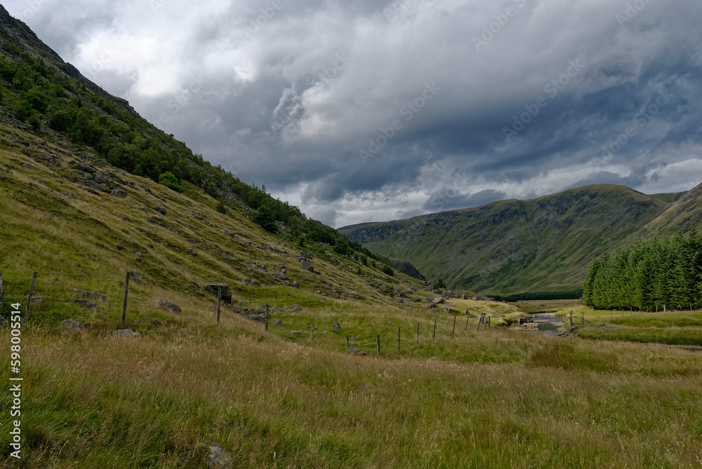 Looking up the Valley from the Footbridge crossing the River South Esk with dark clouds threatening rain on a Summers day in August.