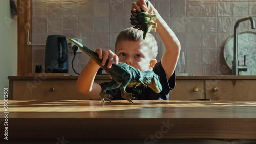 A boy is sitting at a wooden table and playing dinosaurs. Tyrannosaurus rex. Dinosaur duel.