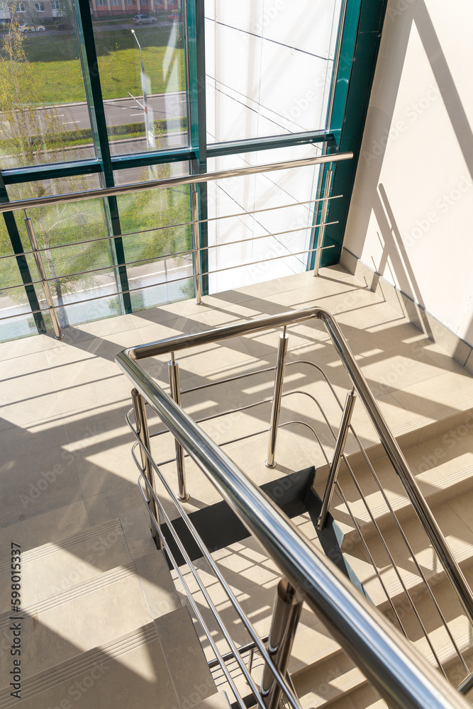 Obraz premium Stairs in a concrete office building in neutral tones, covered with ceramic tiles, with shiny metal railings