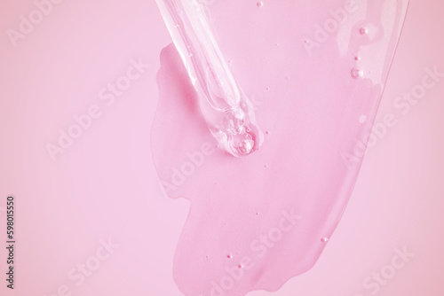 A flowing clear gel from a pipette. Lots of flowing gel smeared on the background. With bubbles. On a pink background.