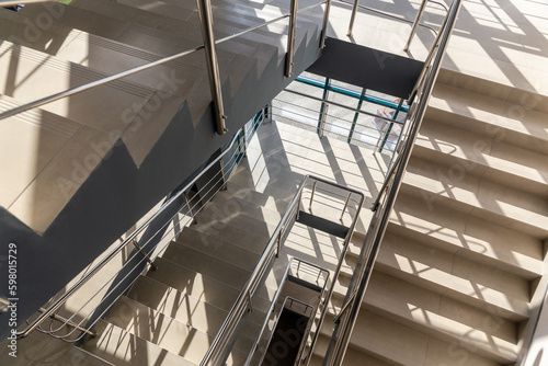 Stairs in a concrete office building in neutral tones, covered with ceramic tiles, with shiny metal railings