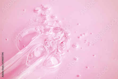 A flowing clear gel from a pipette. A lot of flowing gel in a big drop. With bubbles. On a pink background.