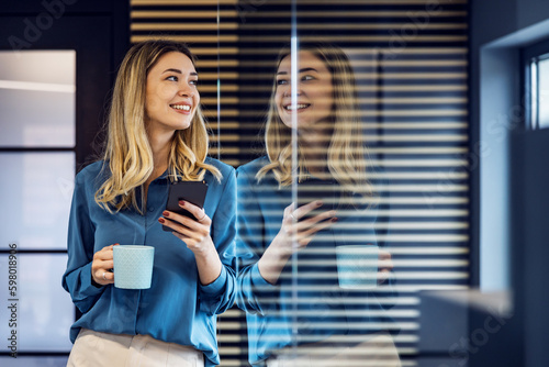 Obraz na płótnie Smiling businesswoman standing in modern office with smart phone