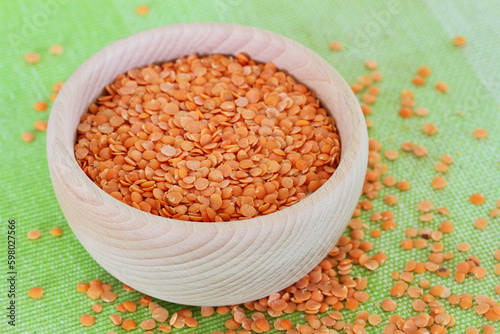 Uncooked red lentils in wooden bowl with lentils scattered on green background
