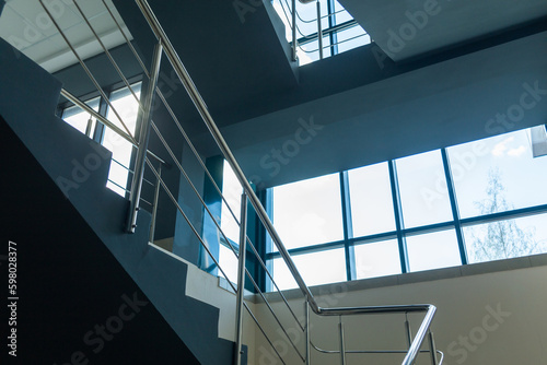 Stairs in a concrete office building in neutral tones, covered with ceramic tiles, with shiny metal railings