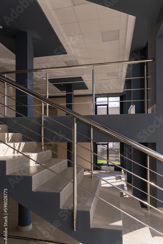 Stairs in a concrete office building in neutral tones, covered with ceramic tiles, with shiny metal railings