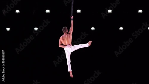 Male, muscular acrobat on Aerial straps on black background performing one arm pull up. Concept of willpower, motivation and passion Generative AI