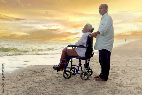 Elderly old senior couple have trip outdoor, happy disabled senior elderly woman in wheelchair travel with her lover on sunset beach, family enjoy spending time, relaxing on summer holiday vacation.