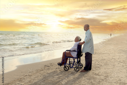 Elderly old senior couple have trip outdoor, happy disabled senior elderly woman in wheelchair travel with her lover on sunset beach, family enjoy spending time, relaxing on summer holiday vacation.