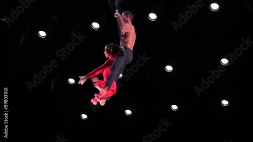 Circus aerial hoop duo on black background performing risky tricks. Man and women fly on stage Generative AI