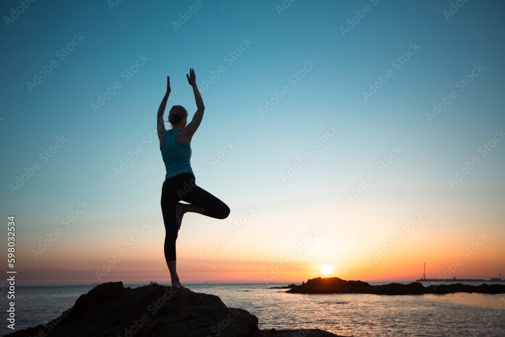 A silhouette of a yoga woman on the ocean shore during sunset.