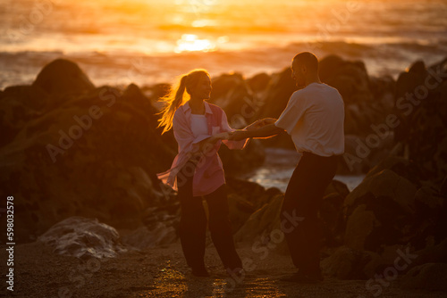 A young couple in love dance on a romantic date on the rocky ocean shore during an amazing sunset. .
