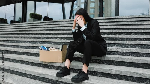 A frustrated woman sits on the stairs outside, feeling the weight of her jobless situation and the struggle to make ends meet. Depressed Woman with Cardboard Box on Stairs Generative AI photo