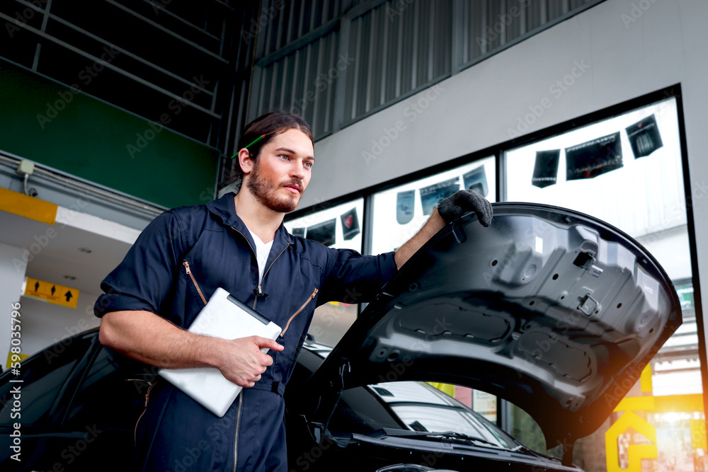 Auto mechanic handsome worker man holding digital tablet and working at garage, car service technician checking and repairing customer car at automobile service center, vehicle repair service shop. Auto mechanic handsome worker man holding digital tablet and working at garage, car service technician checking and repairing customer car at automobile service center, vehicle repair service shop.