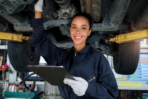 Beautiful female auto mechanic checking wheel tires in garage, car service technician woman repairing customer car at automobile service, inspecting vehicle underbody and suspension engine system.