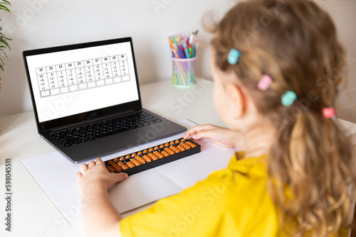 A girl from the back is engaged in mental arithmetic on the abacus online on a laptop, chroma key background. The concept of teaching children to count quickly, Russian mathematics. photo